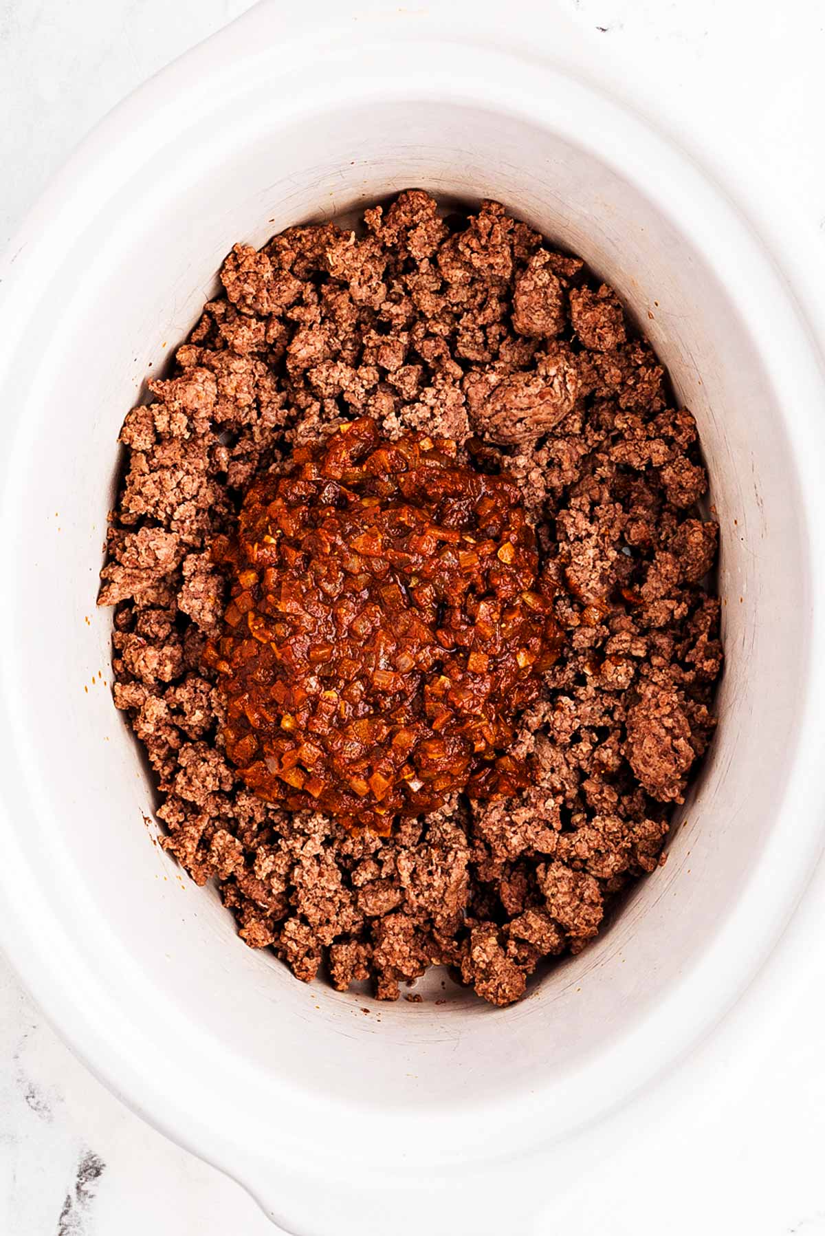 overhead view of chili base mixture in slow cooker on top of browned ground beef