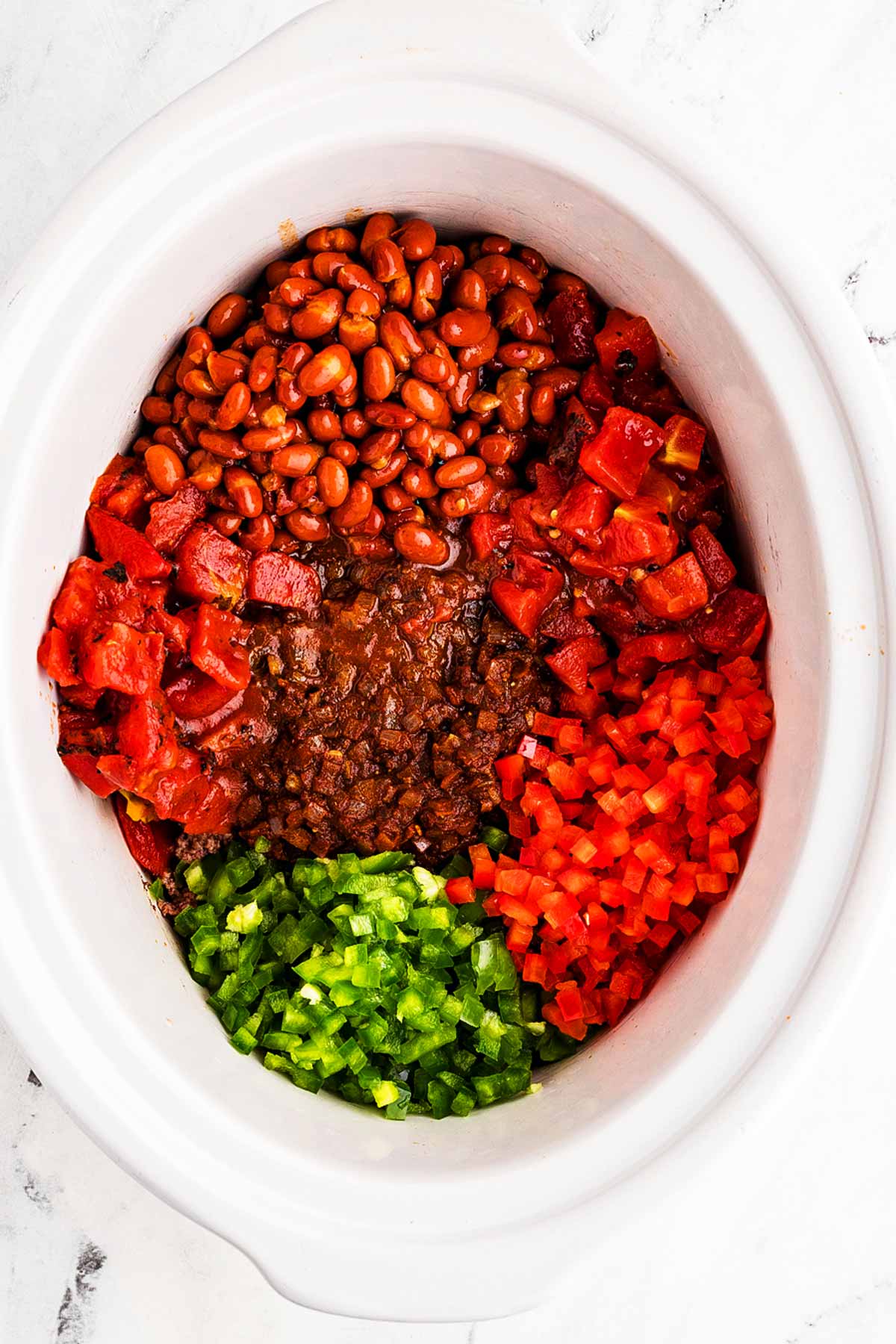 overhead view of diced red and green bell peppers, chili beans and diced tomatoes added to slow cooker