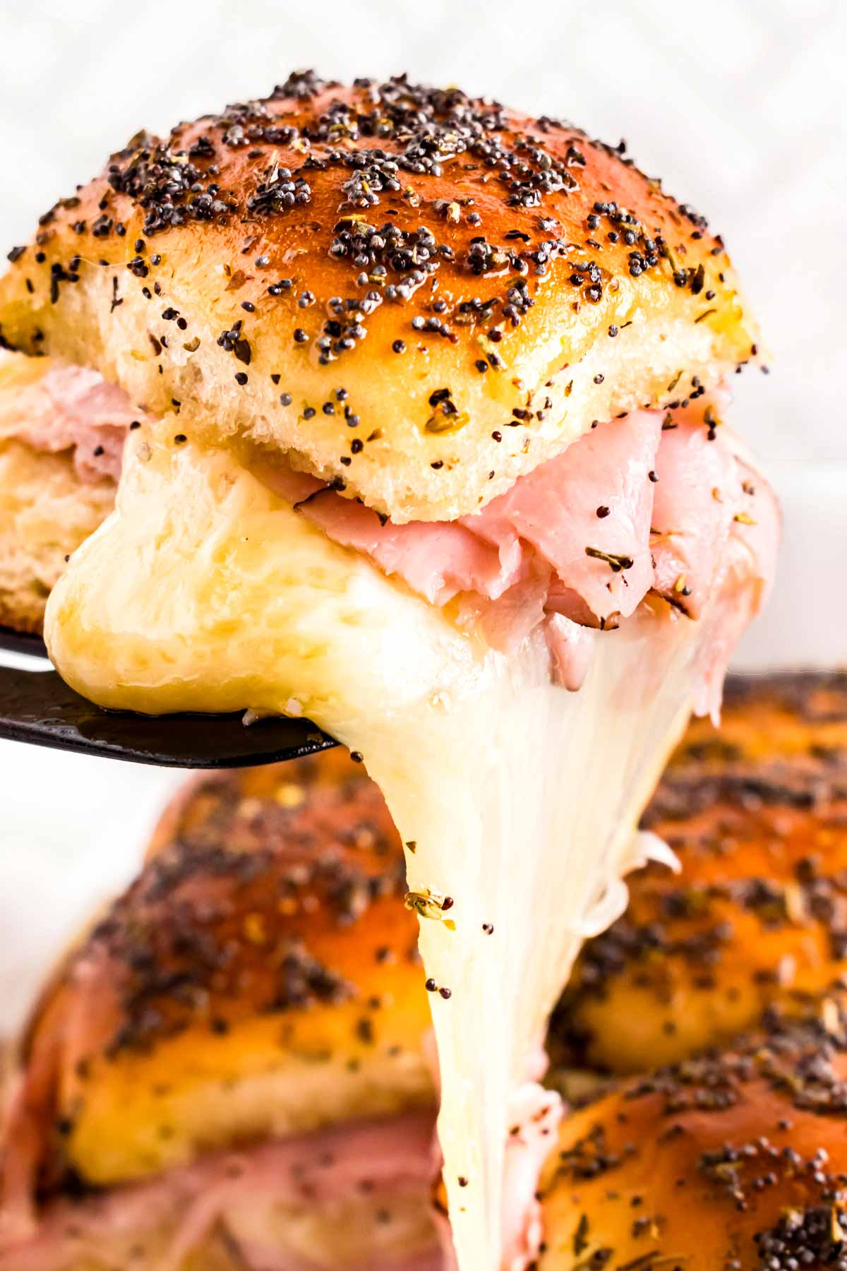 frontal view of cheesy ham slider being pulled from slab of rolls