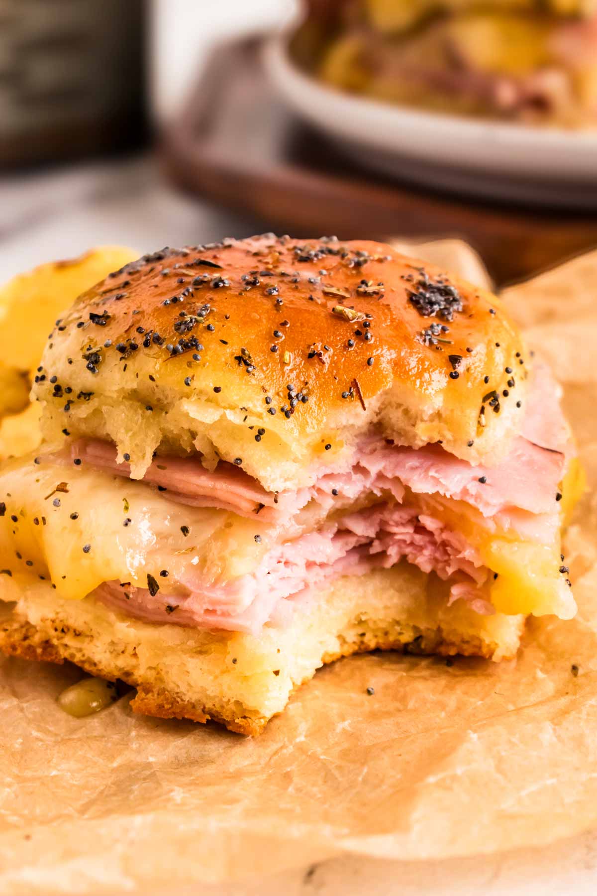 frontal view of hot garlic herb ham slider on parchment paper with a bite taken out