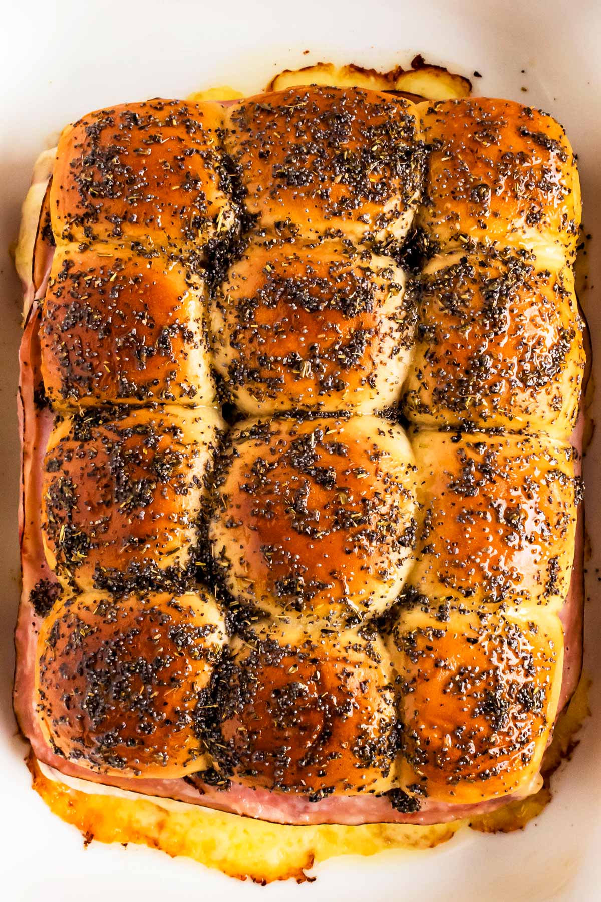 overhead view of baked ham sliders brushed with garlic herb butter in white casserole dish