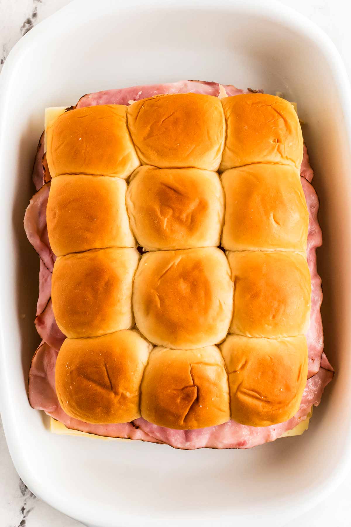 overhead view of unbaked ham sliders in white casserole dish