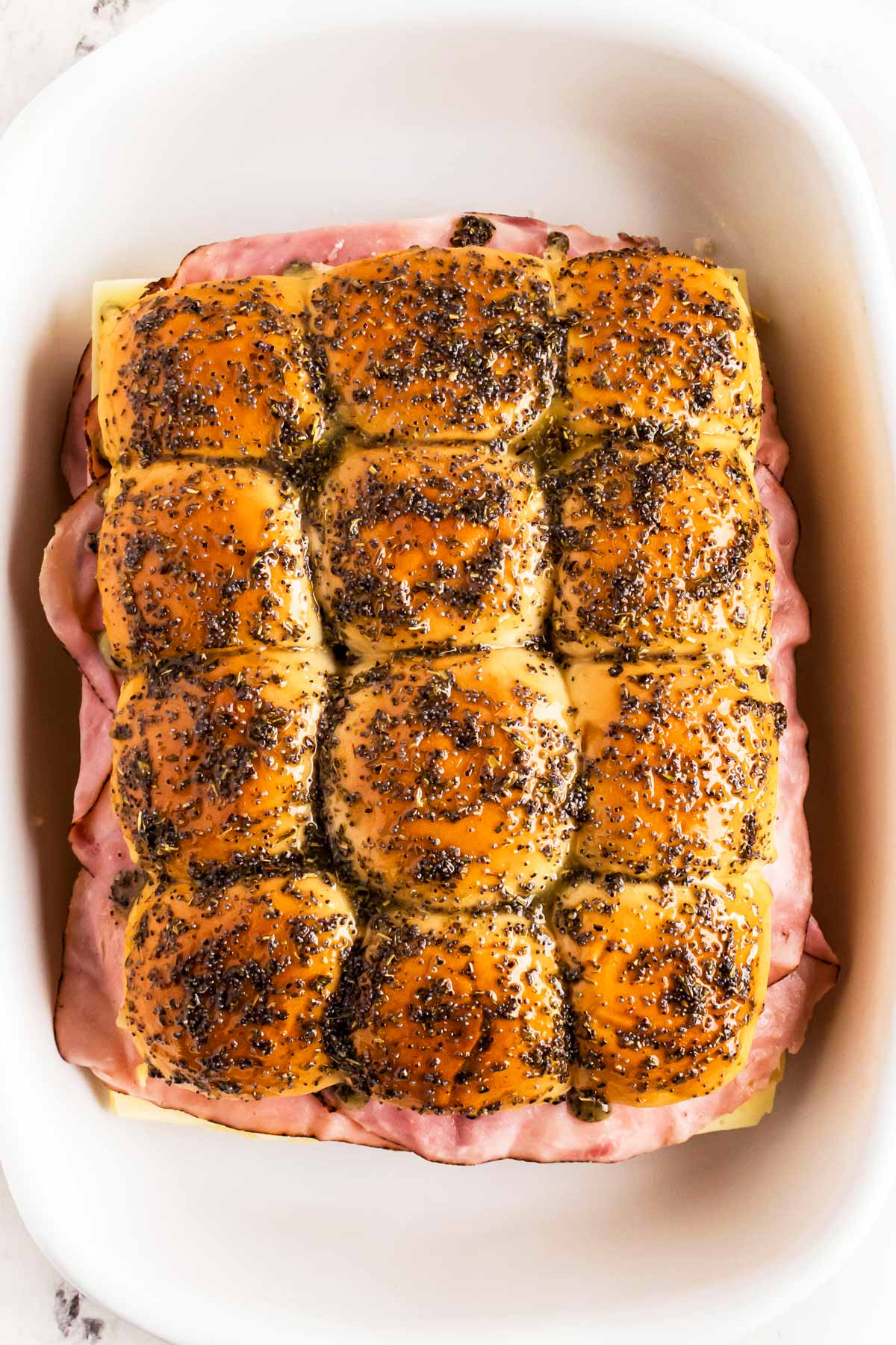 overhead view of unbaked ham sliders brushed with garlic herb butter in white casserole dish