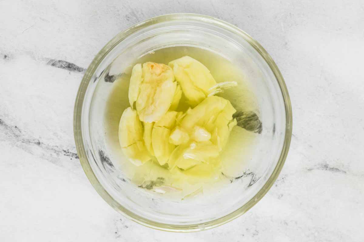 overhead view of smashed garlic in bowl with pepperoncini juice