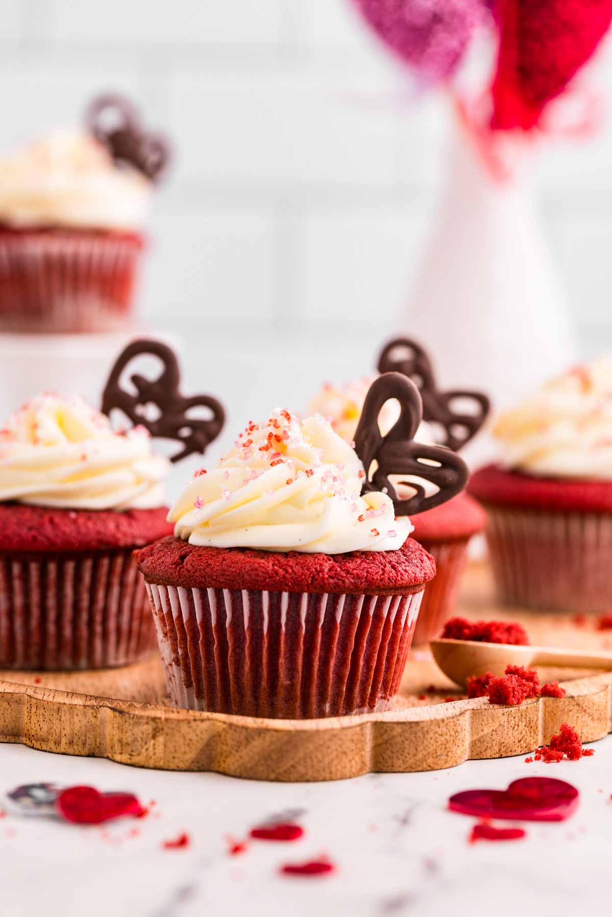 frontal view of red velvet cupcakes with Valentine's Day decor in the back