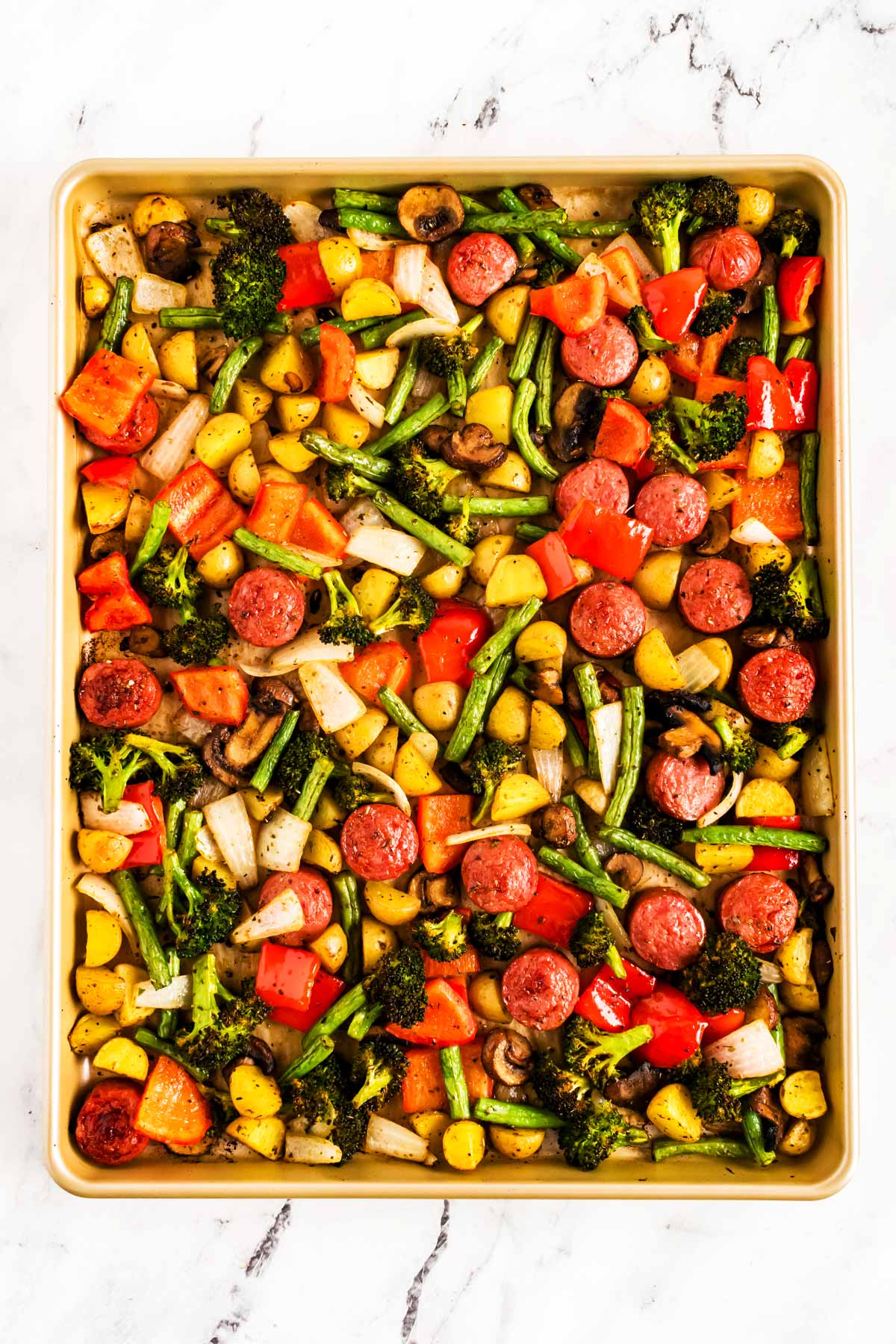 overhead view of roasted vegetables and sausage slices on sheet pan