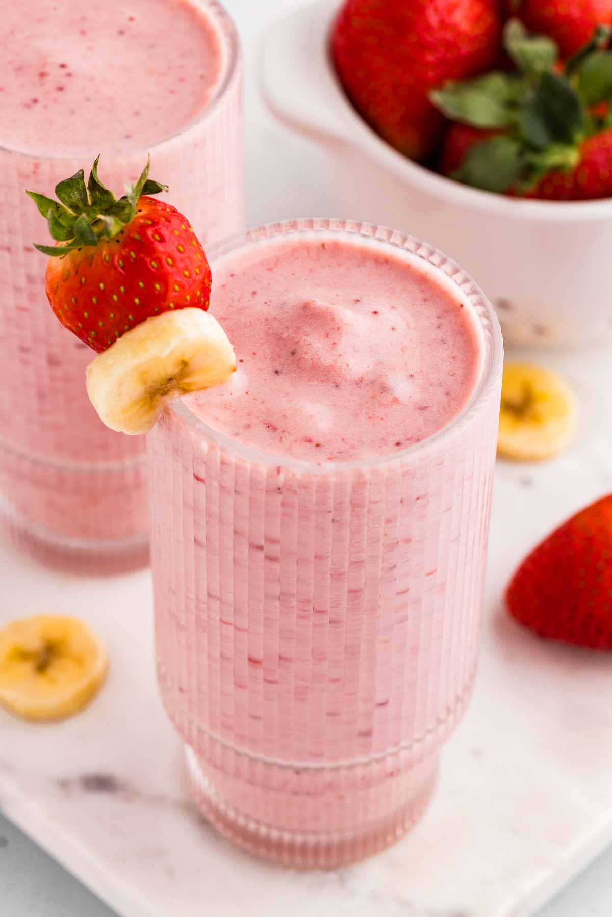 angled frontal view of glasses filled with strawberry banana smoothie garnished with banana and strawberries