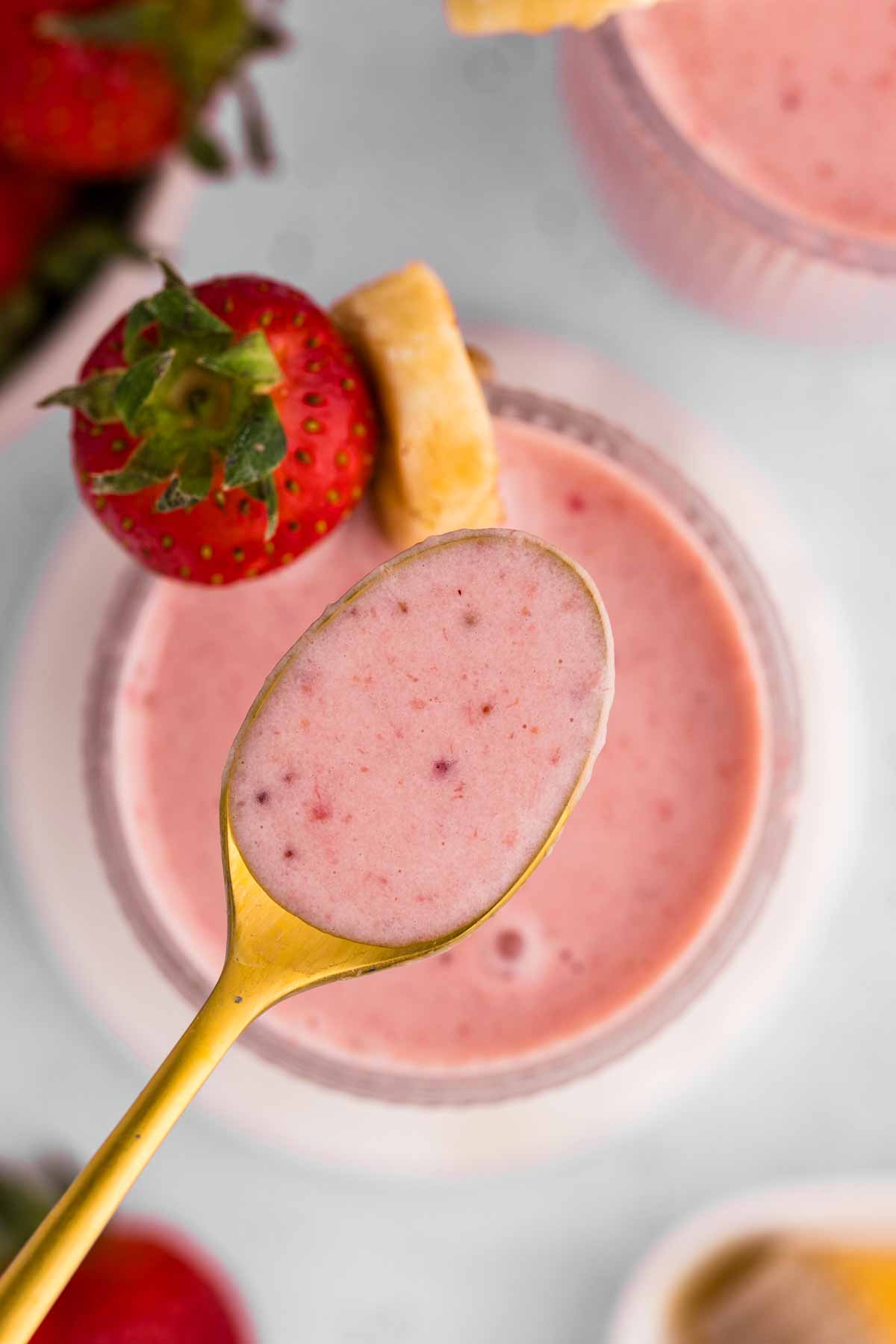 overhead view of spoon spooning strawberry banana smoothie from glass