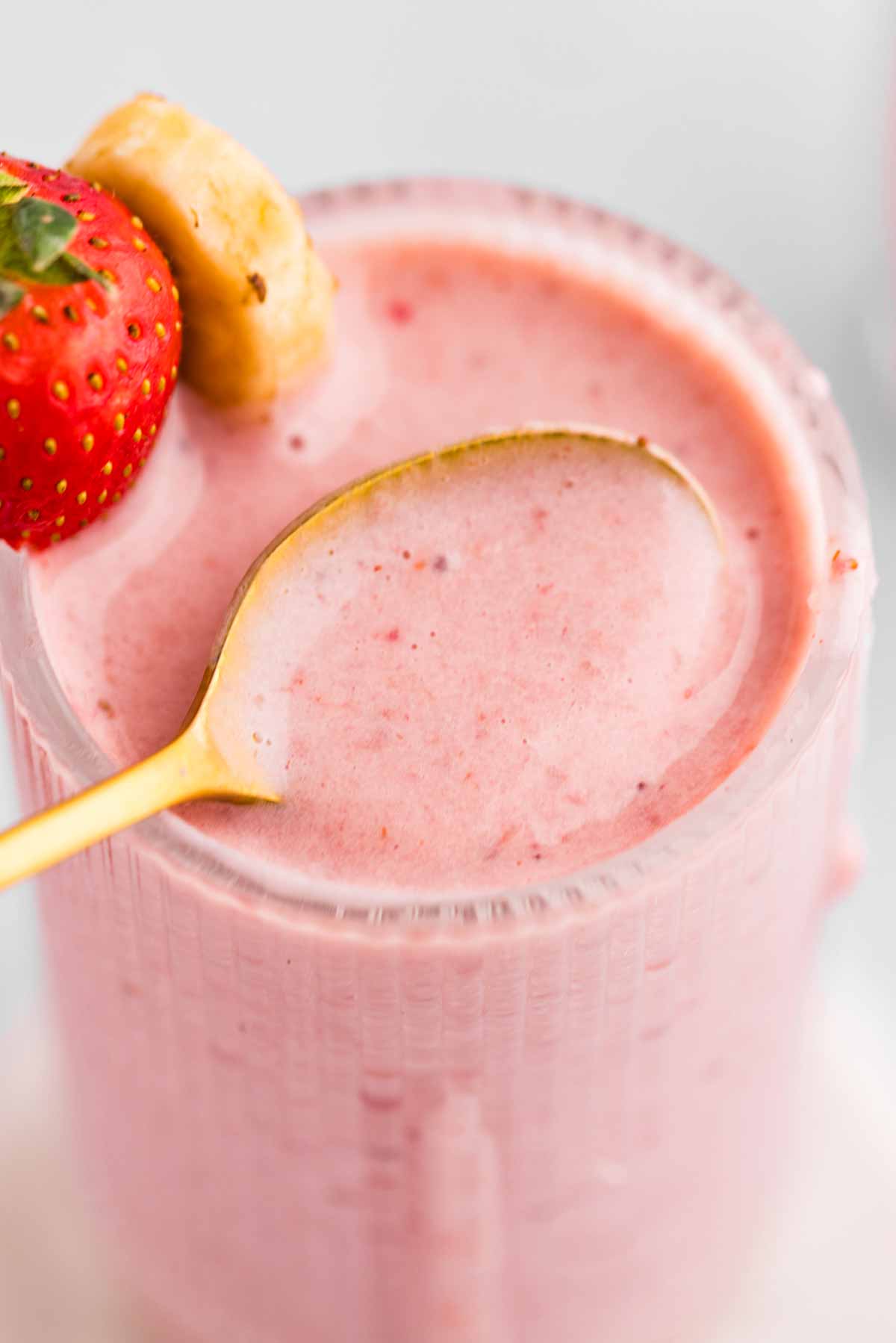 frontal close up view of strawberry banana smoothie in glass with golden spoon