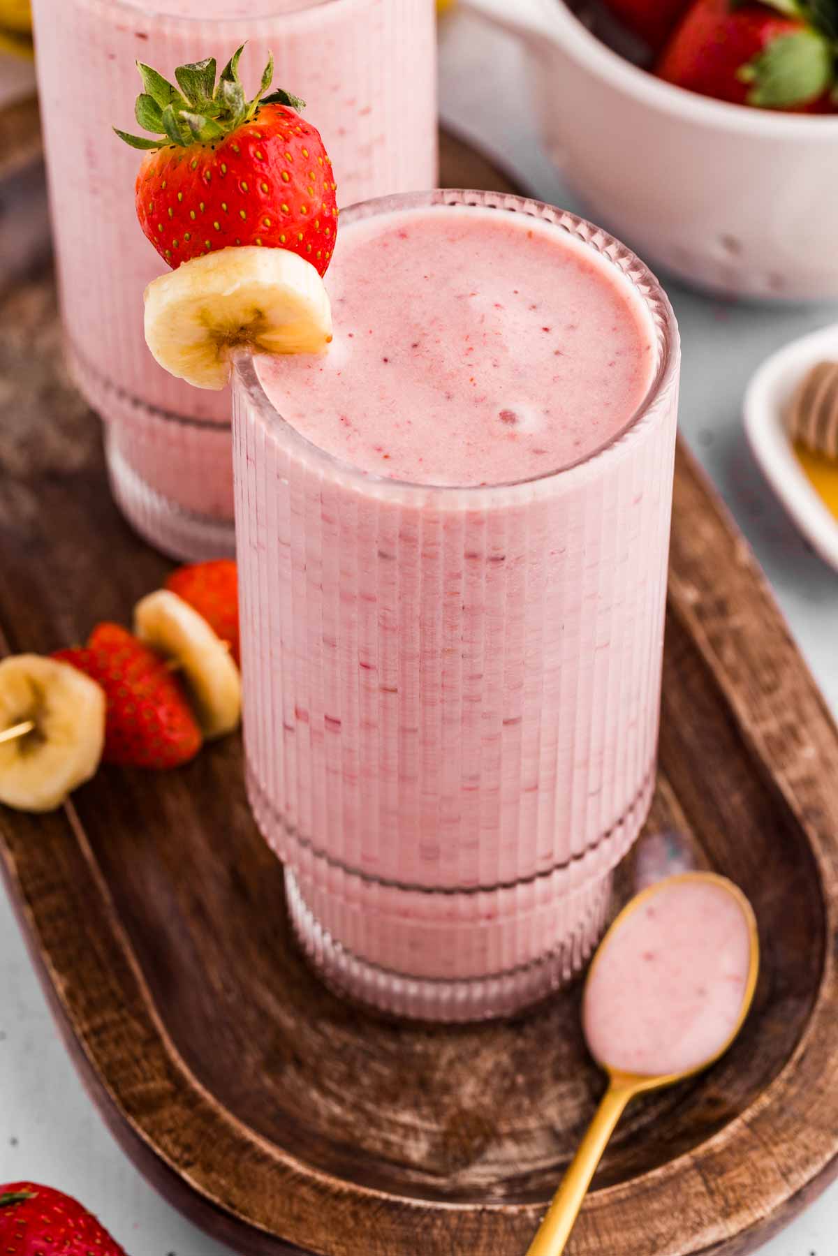 frontal view of glass filled with strawberry banana smoothie on wooden board