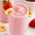 angled frontal view of glasses filled with strawberry banana smoothie garnished with banana and strawberries