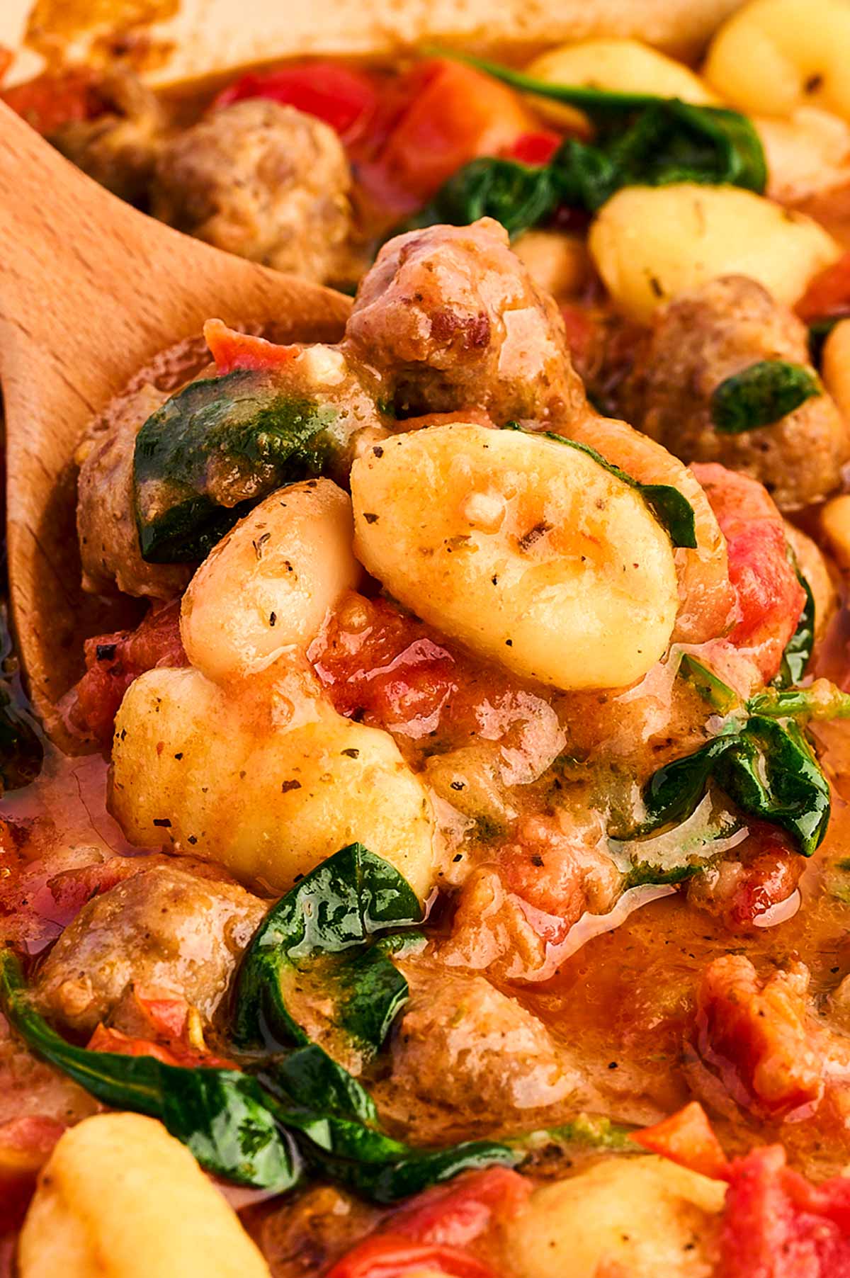 frontal close up view of sausage gnocchi on wooden spoon