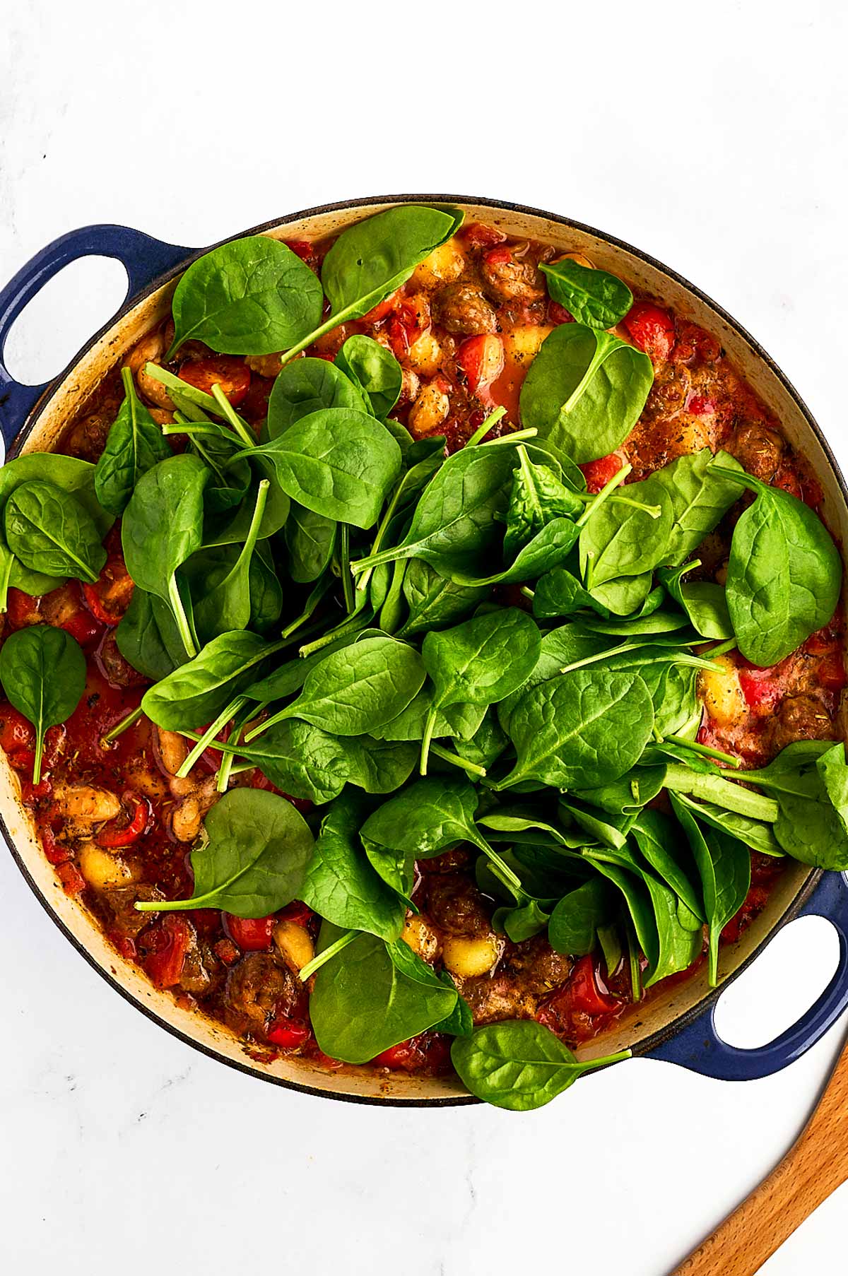 overhead view of fresh baby spinach stirred into baked gnocchi mixture in dutch oven