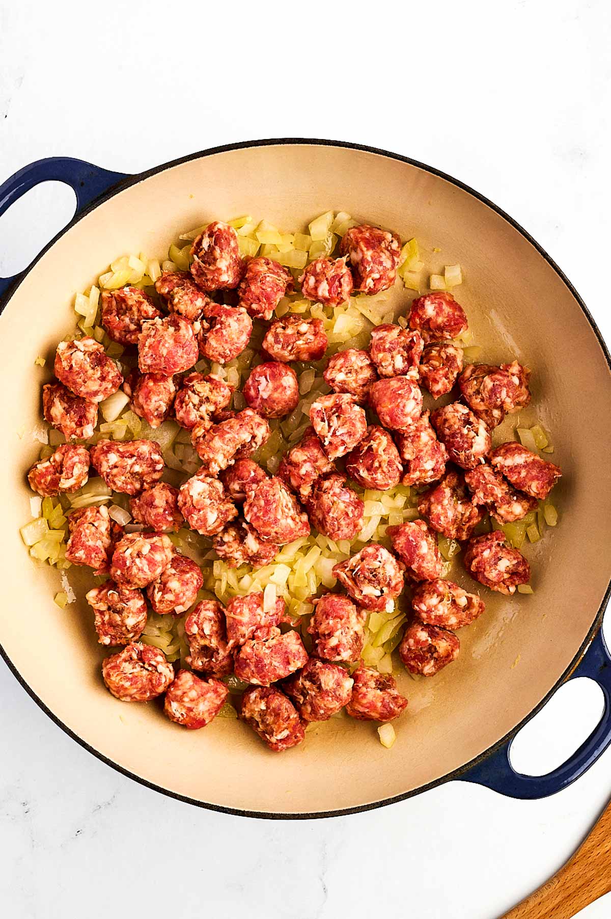 overhead view of uncooked sausage chunks added to softened onion in dutch oven