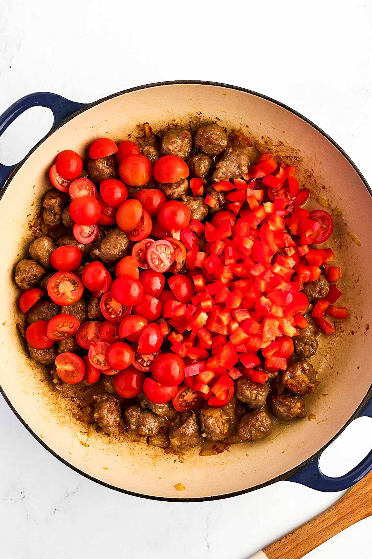 overhead view of halved cherry tomatoes and diced red bell pepper added to sausage mixture in dutch oven