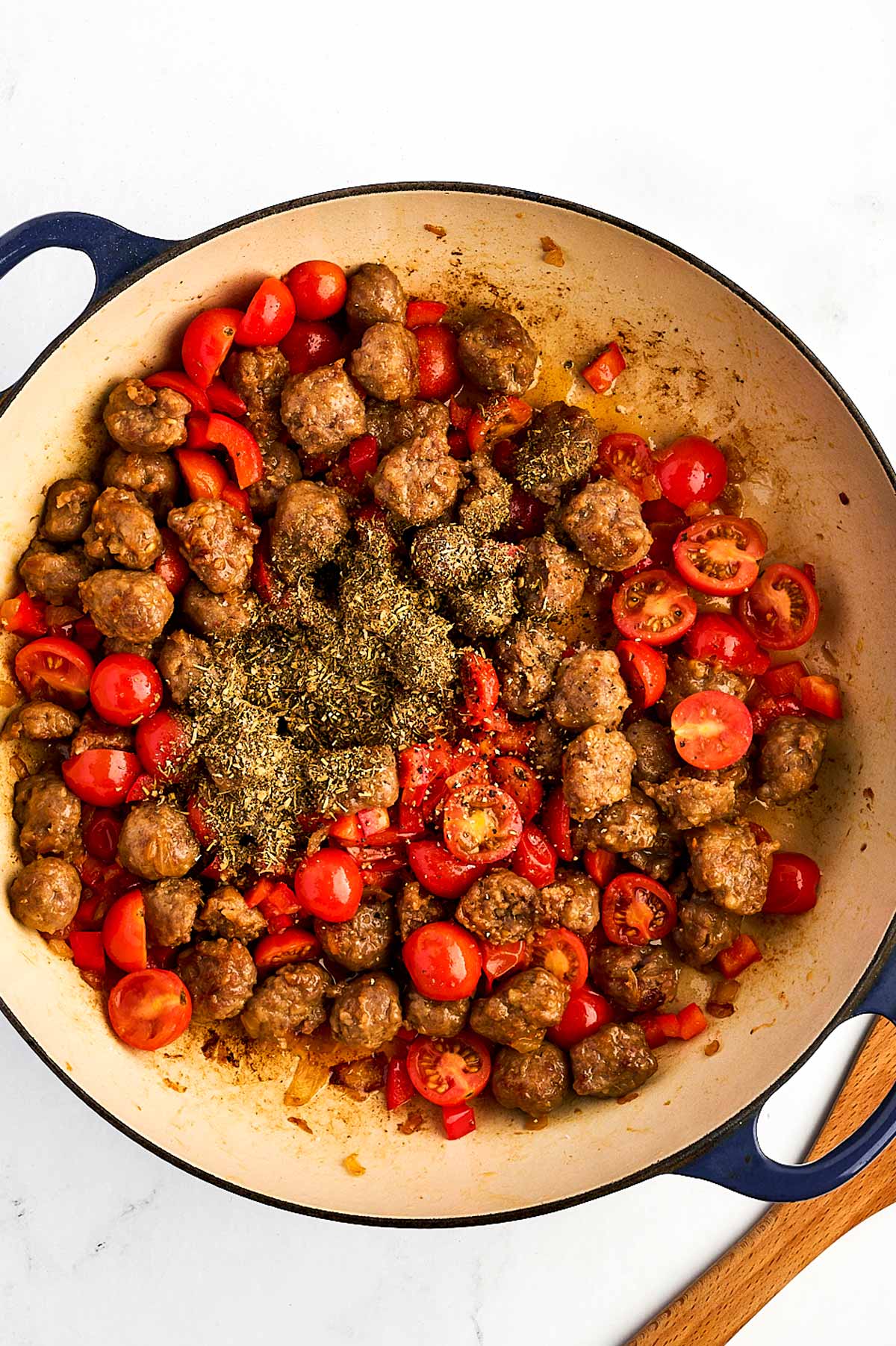 overhead view of softened cherry tomatoes and red bell peppers cooking with sausage mixture and spices