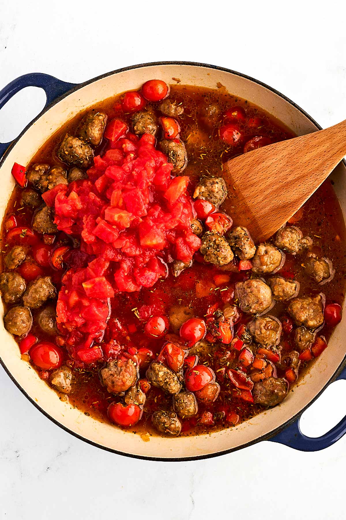 overhead view of diced tomatoes and water added to sausage and vegetable mixture in dutch oven