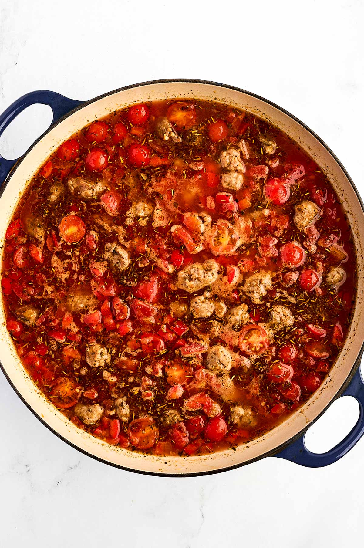 overhead view of sausage in tomato sauce simmering in Dutch oven