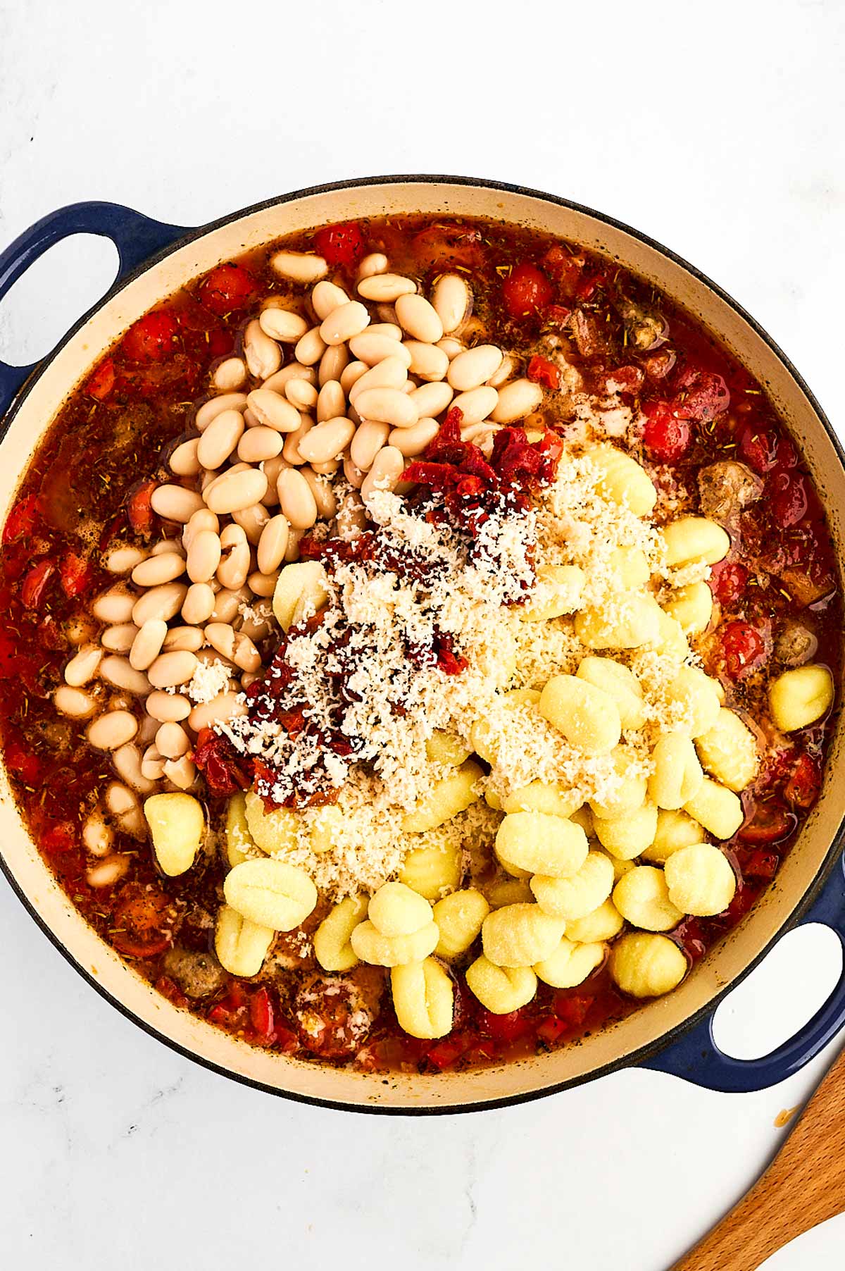 overhead view of uncooked gnocchi added to sauce with beans and sausage