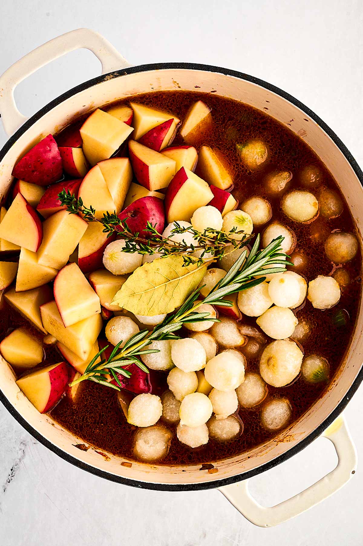 overhead view of potatoes and pearl onions on top of gravy in Dutch oven