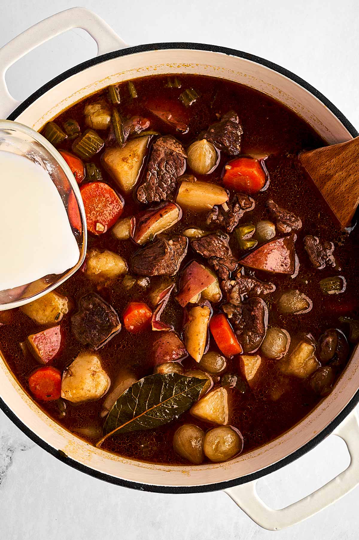 overhead view of cornstarch slurry poured into beef stew in Dutch oven