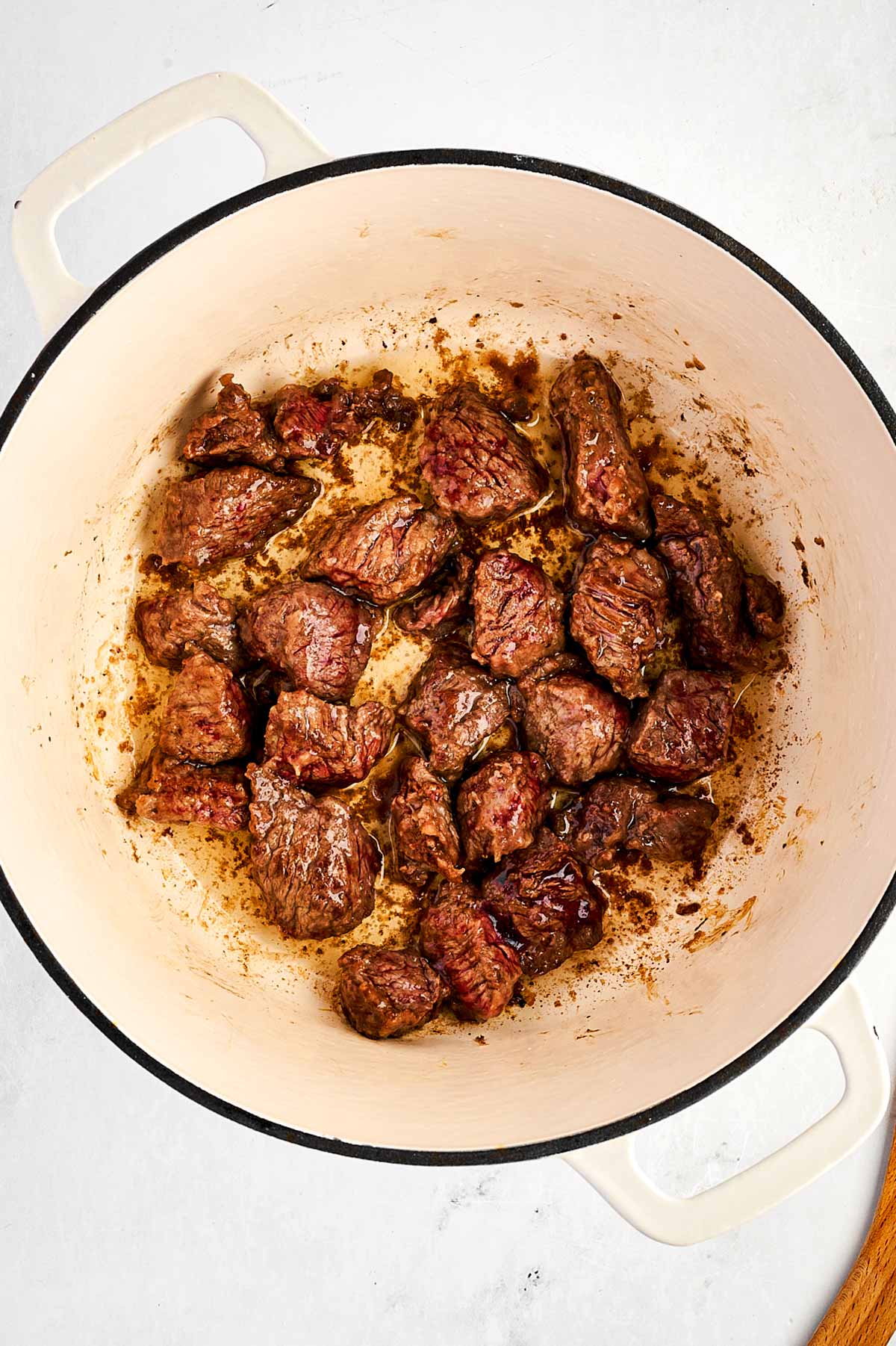 overhead view of browned beef cubes in white Dutch oven