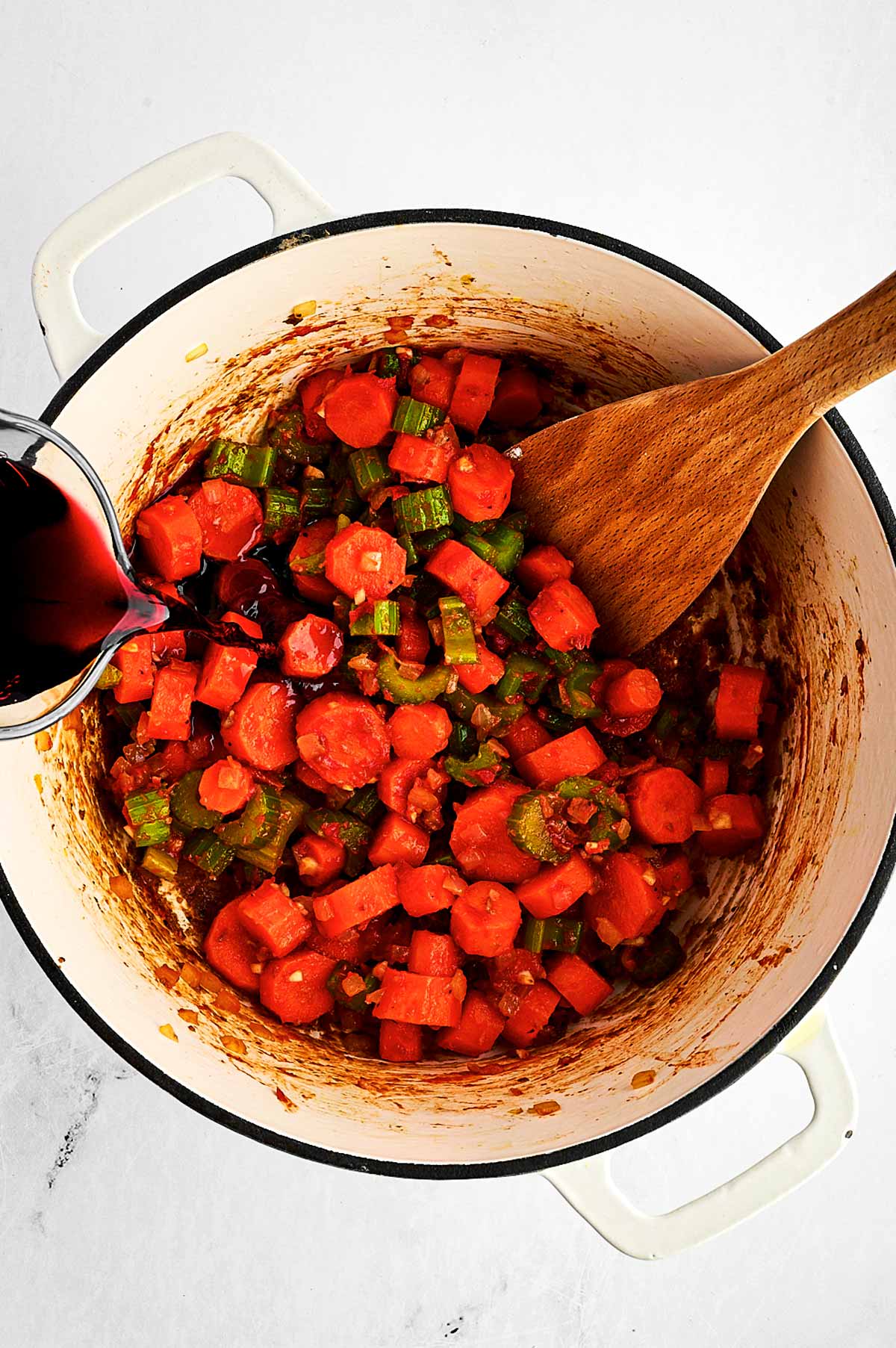 overhead view of red wine being poured over vegetables in Dutch oven