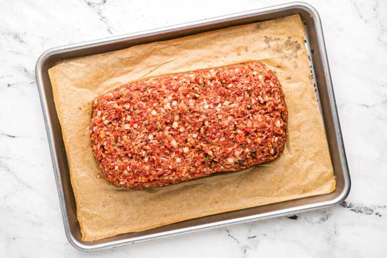 overhead view of unglazed and unbaked meatloaf on parchment p lined baking pan