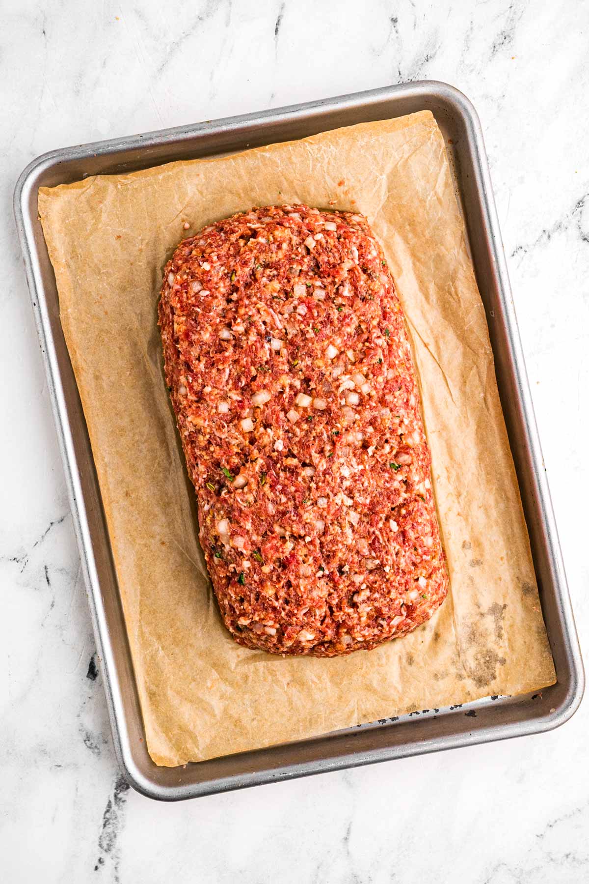 overhead view of unglazed and unbaked meatloaf on parchment p
lined baking pan