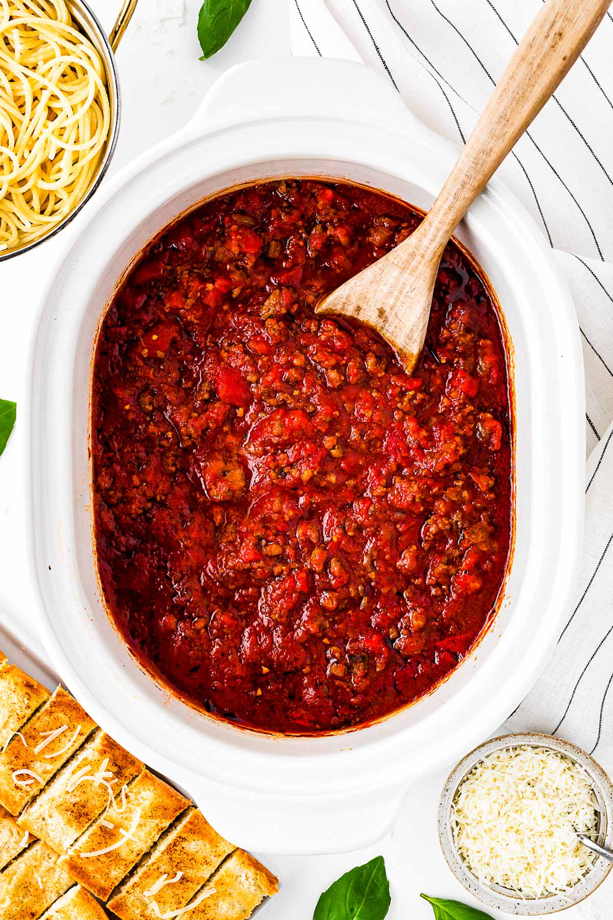 overhead view of cooked spaghetti sauce in slow cooker surrounded by pasta and garlic bread