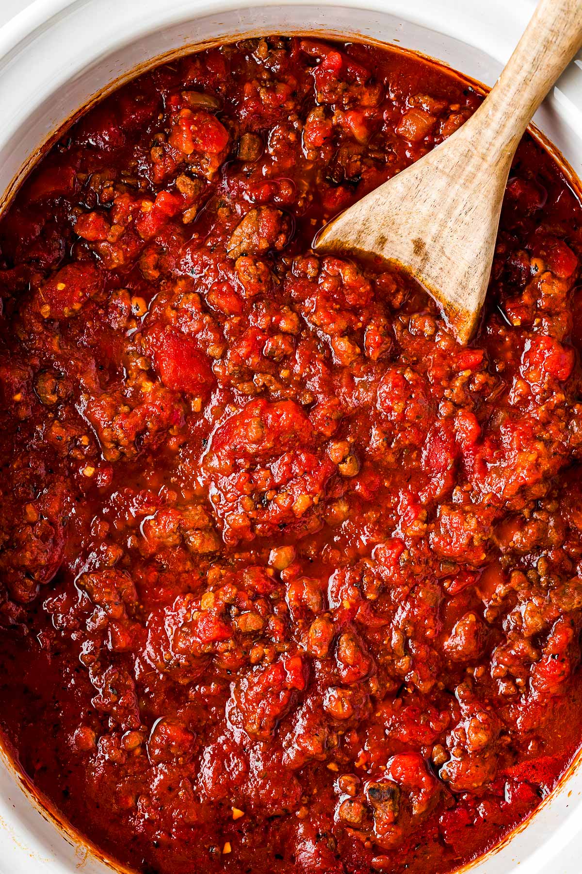 overhead view of spaghetti sauce in crock pot with wooden spoon