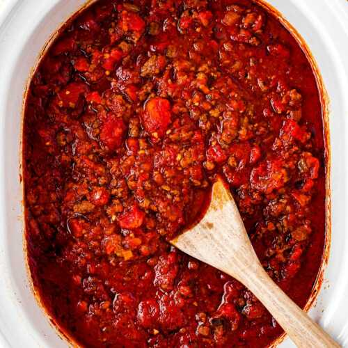 overhead view of spaghetti sauce in crock pot with wooden spoon