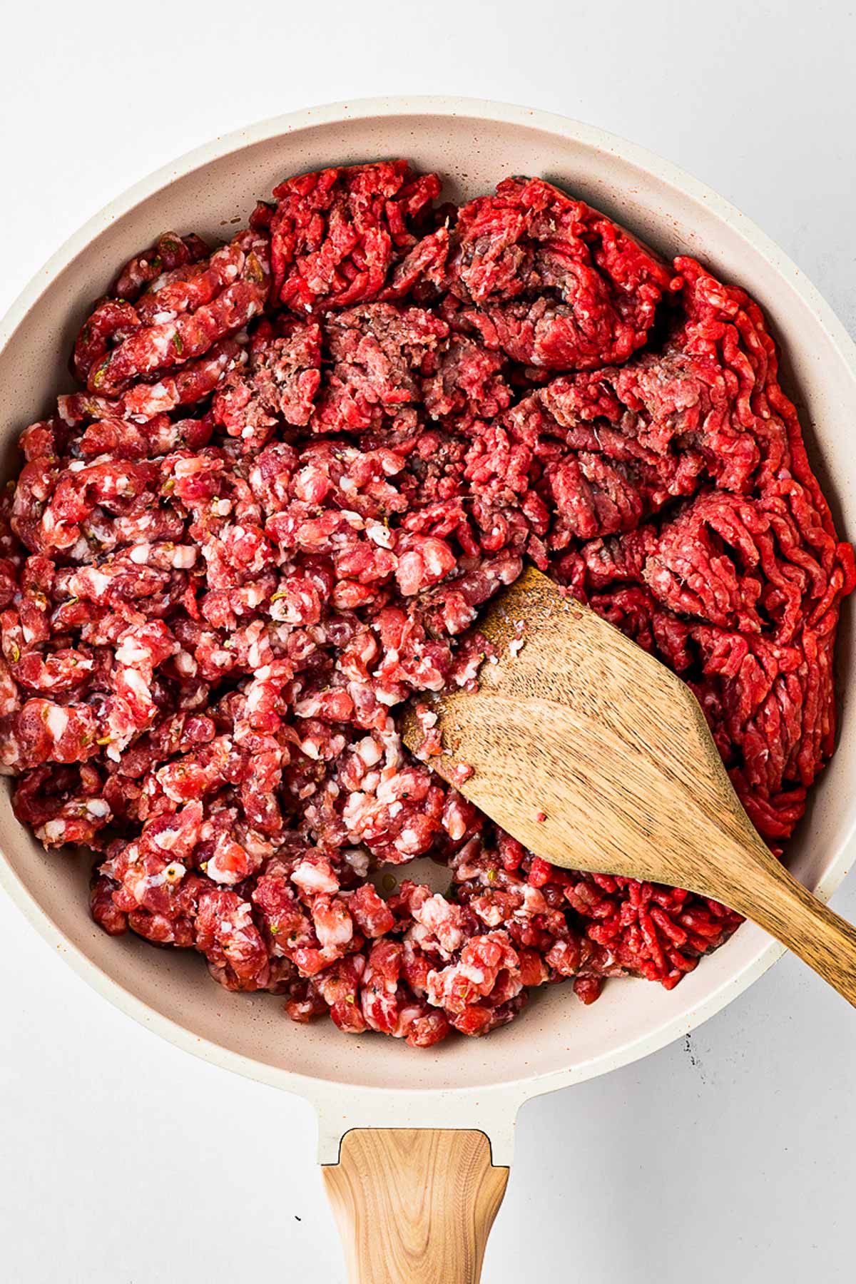 overhead view of raw ground beef and sausage in skillet with oil