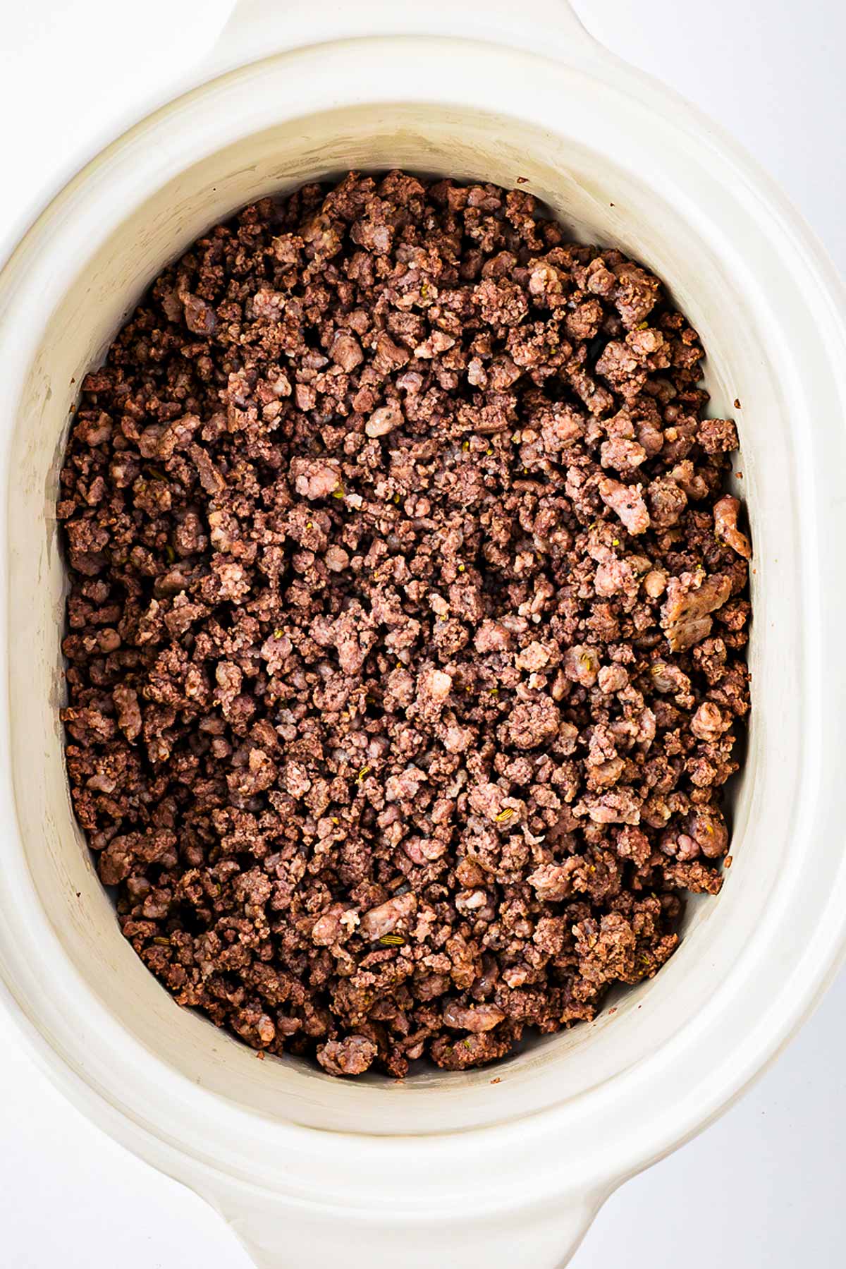 overhead view of cooked ground beef and sausage transferred to slow cooker