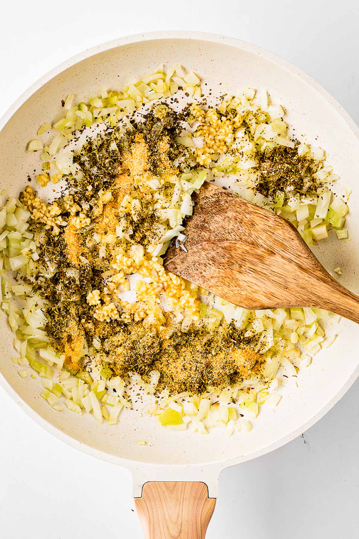 overhead view of spices added to skillet with onions and garlic