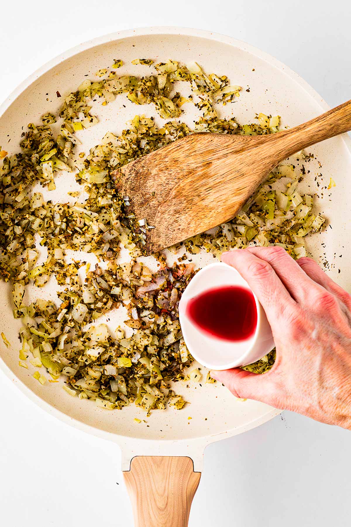 overhead view of female hand pouring red wine into skillet with cooked onion