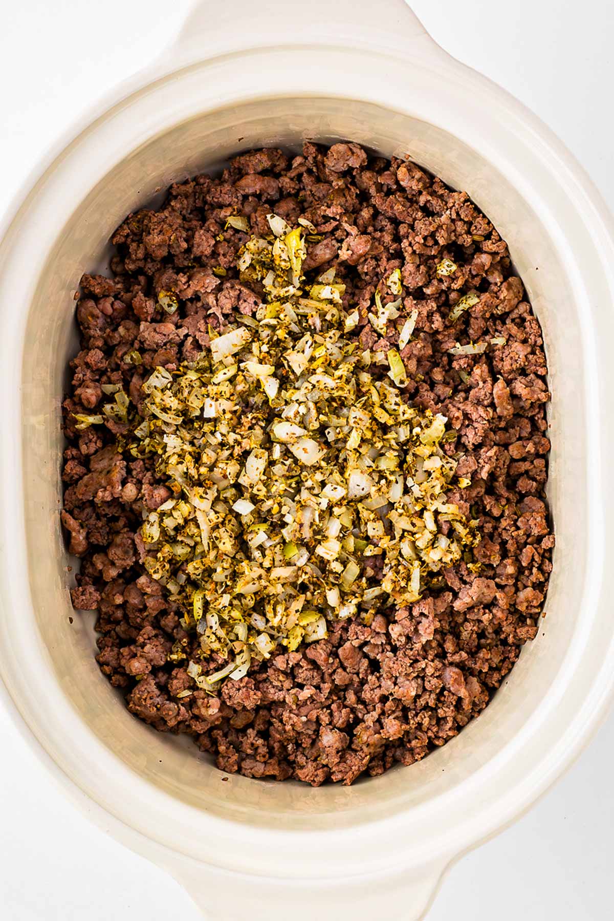 overhead view of slow cooker with cooked meat and deglazed onions added