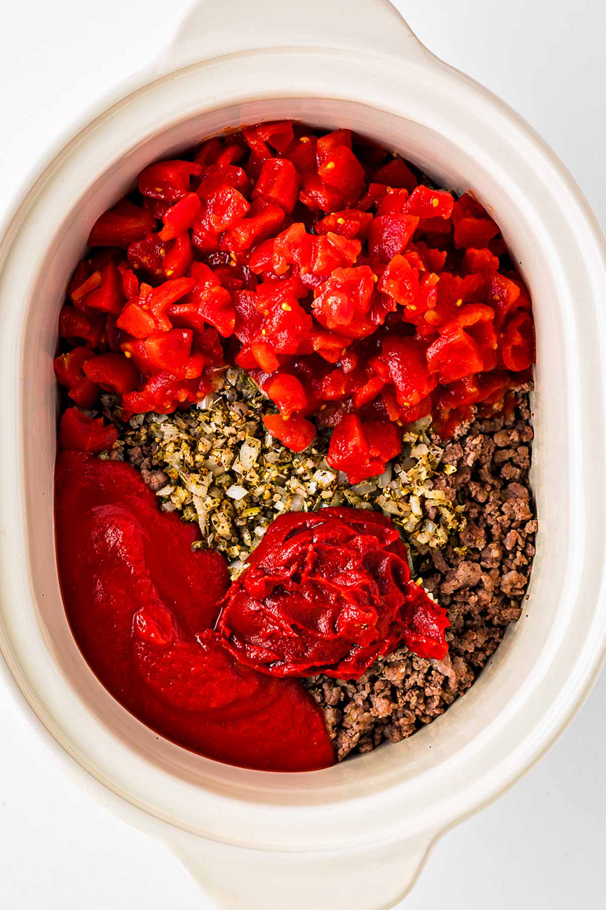 overhead view of tomatoes and seasoning being in white slow cooker