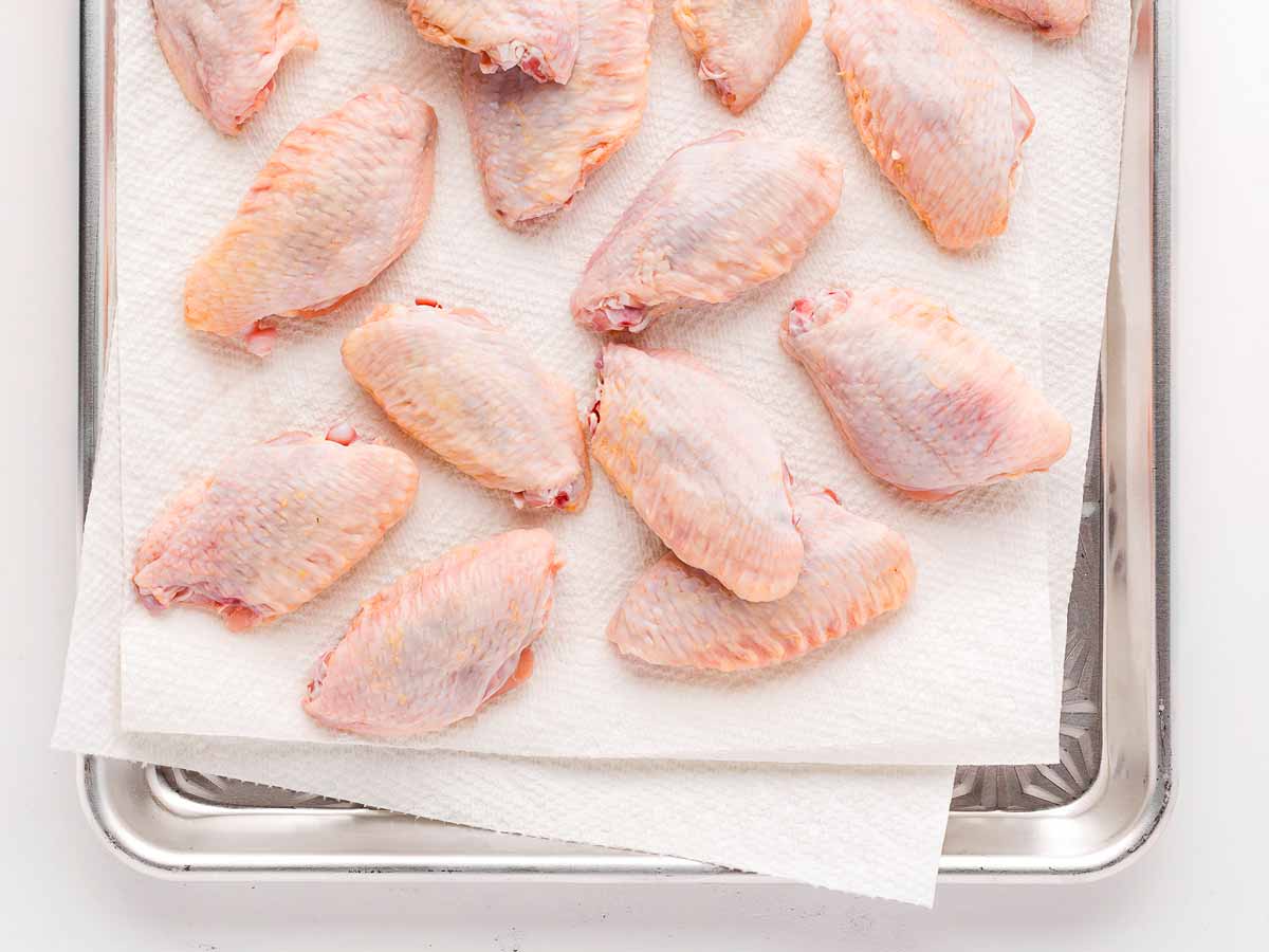 overhead view of raw chicken wings on paper towels, being patted dry