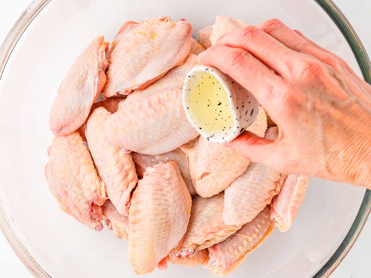 overhead view of chicken wings in large bowl female hand pouring over oil