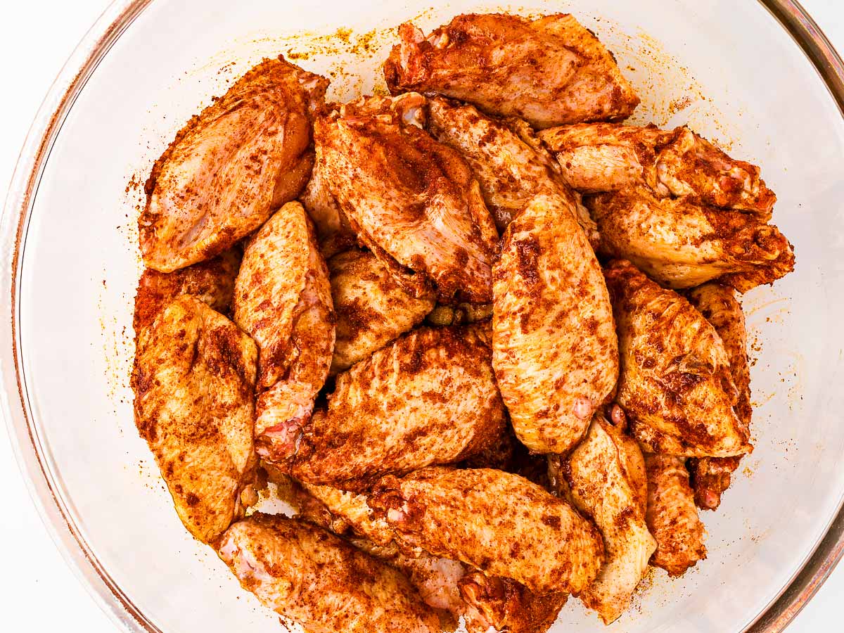 overhead view of seasoned chicken wings being tossed in bowl