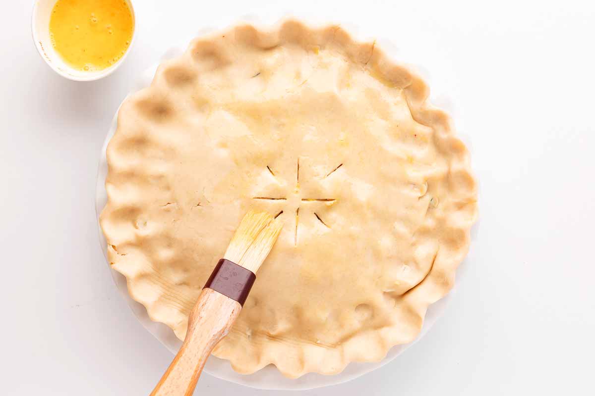 overhead shot of egg wash being brushed onto the top crust