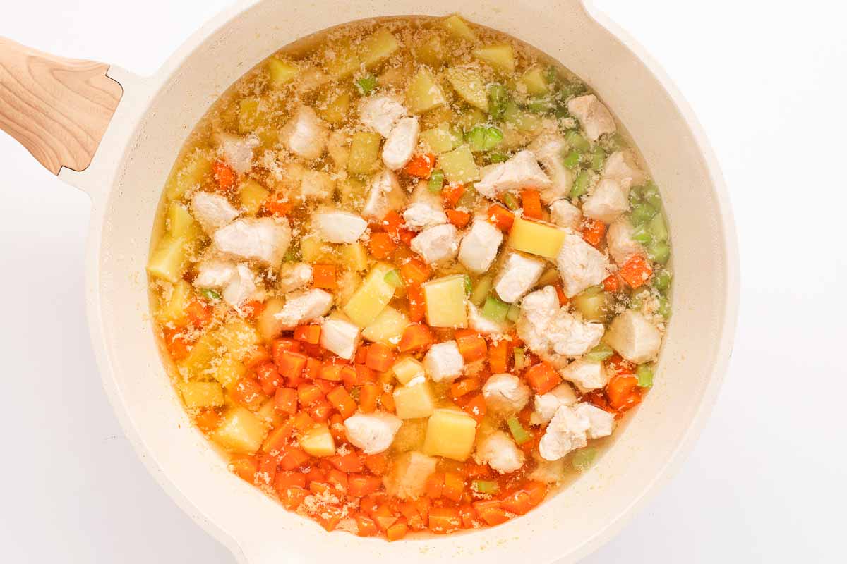 overhead shot of chicken and vegetables simmering in broth in a pot