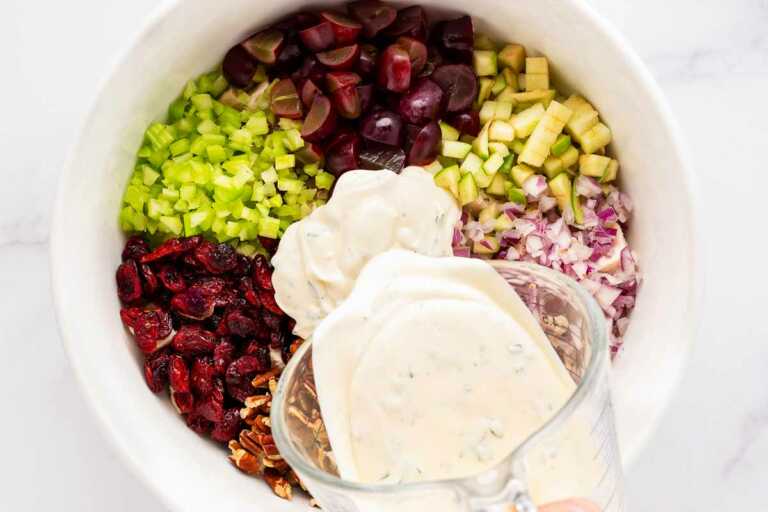 overhead view of creamy dressing being poured over chicken salad ingredients in bowl