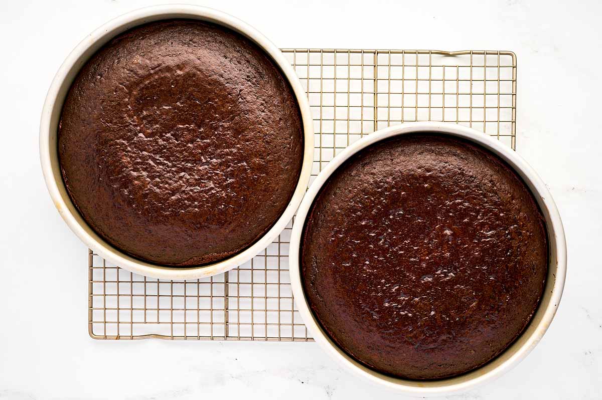 overhead view of two baked chocolate cakes in cake pans on wire rack