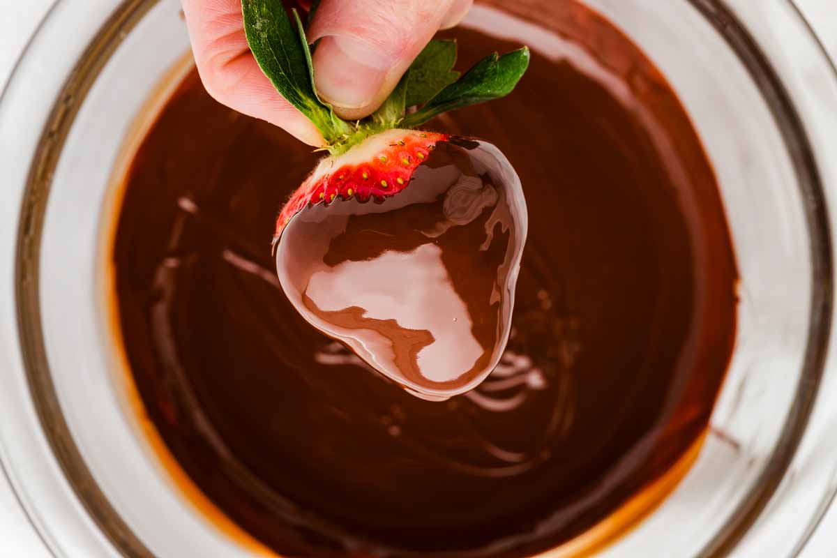 overhead view of female hand dipping strawberry in chocolate