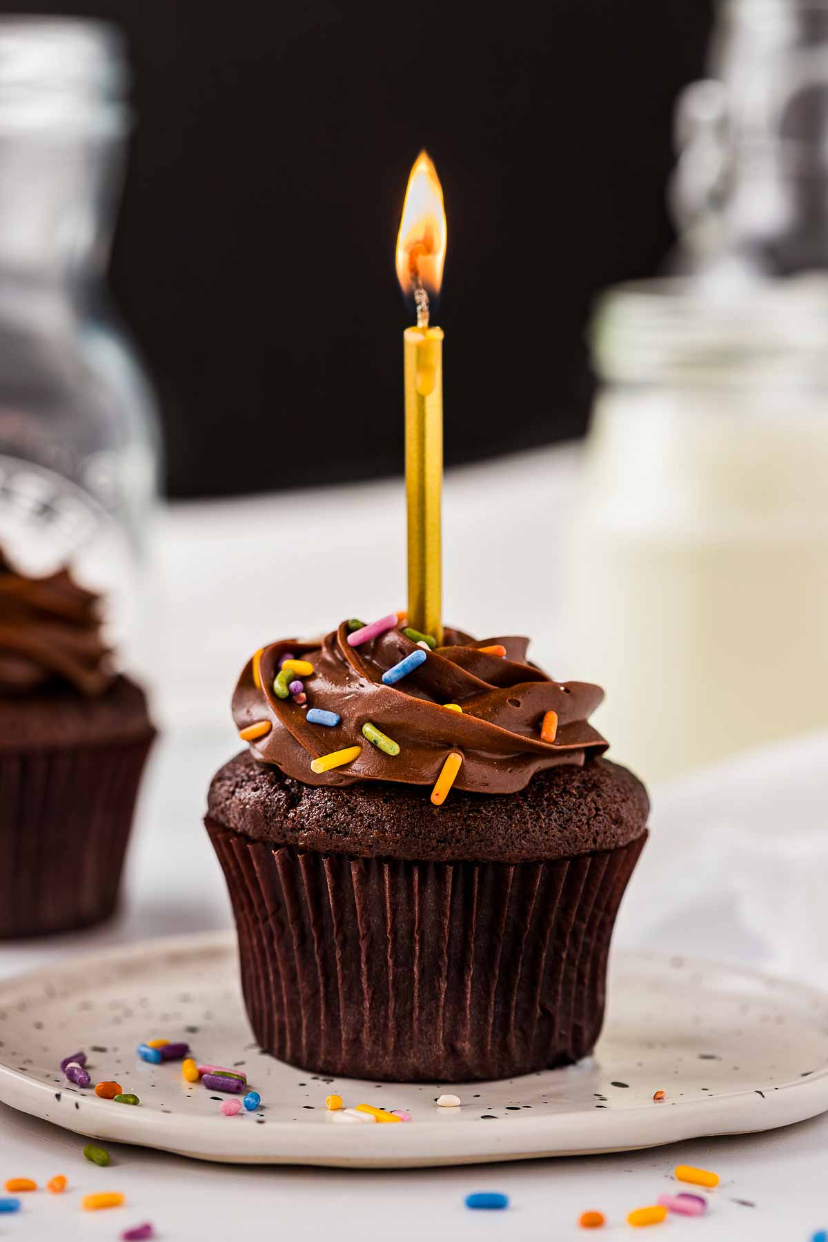 frontal view of chocolate cupcake with birthday sprinkles and burning candle