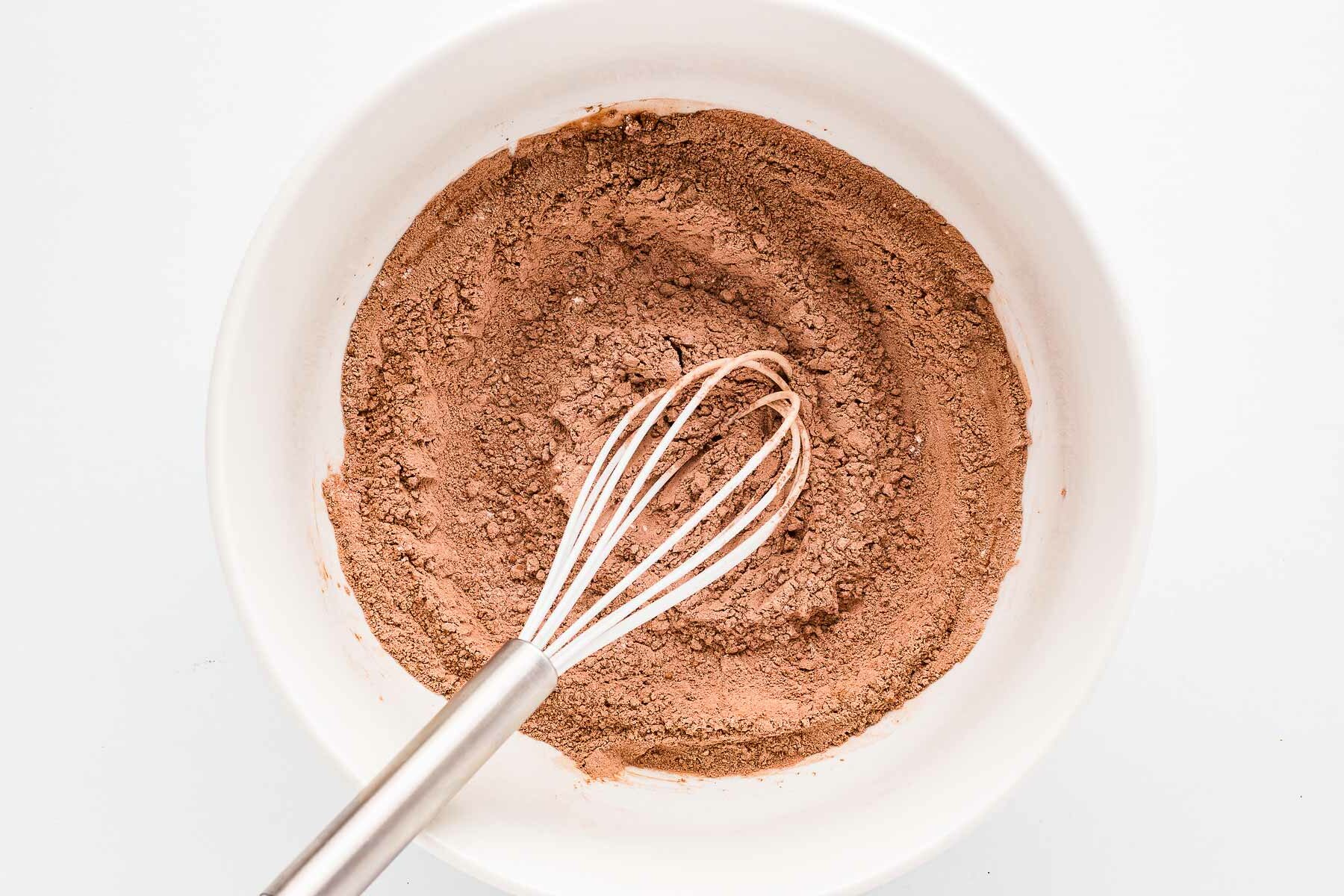 overhead view of dry ingredients for chocolate cupcakes combined in bowl with whisk