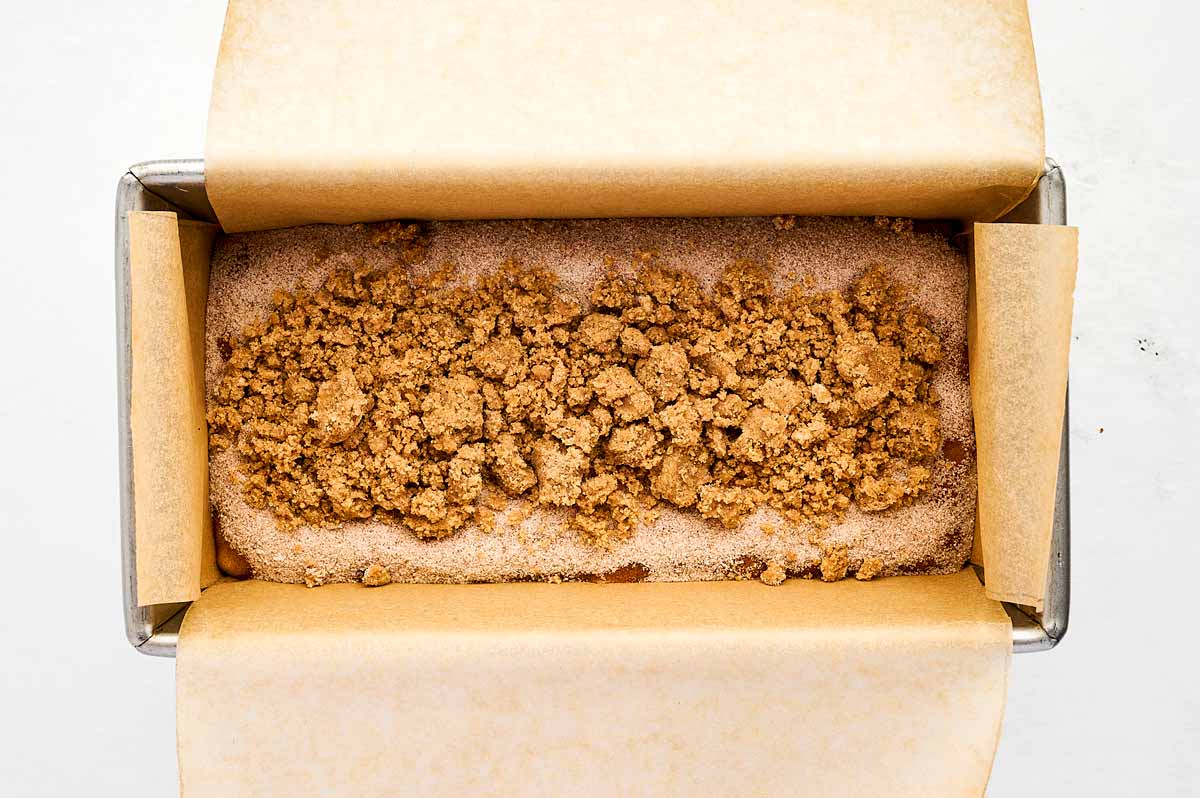 overhead view of banana bread batter in lined loaf pan topped with cinnamon sugar and streusel