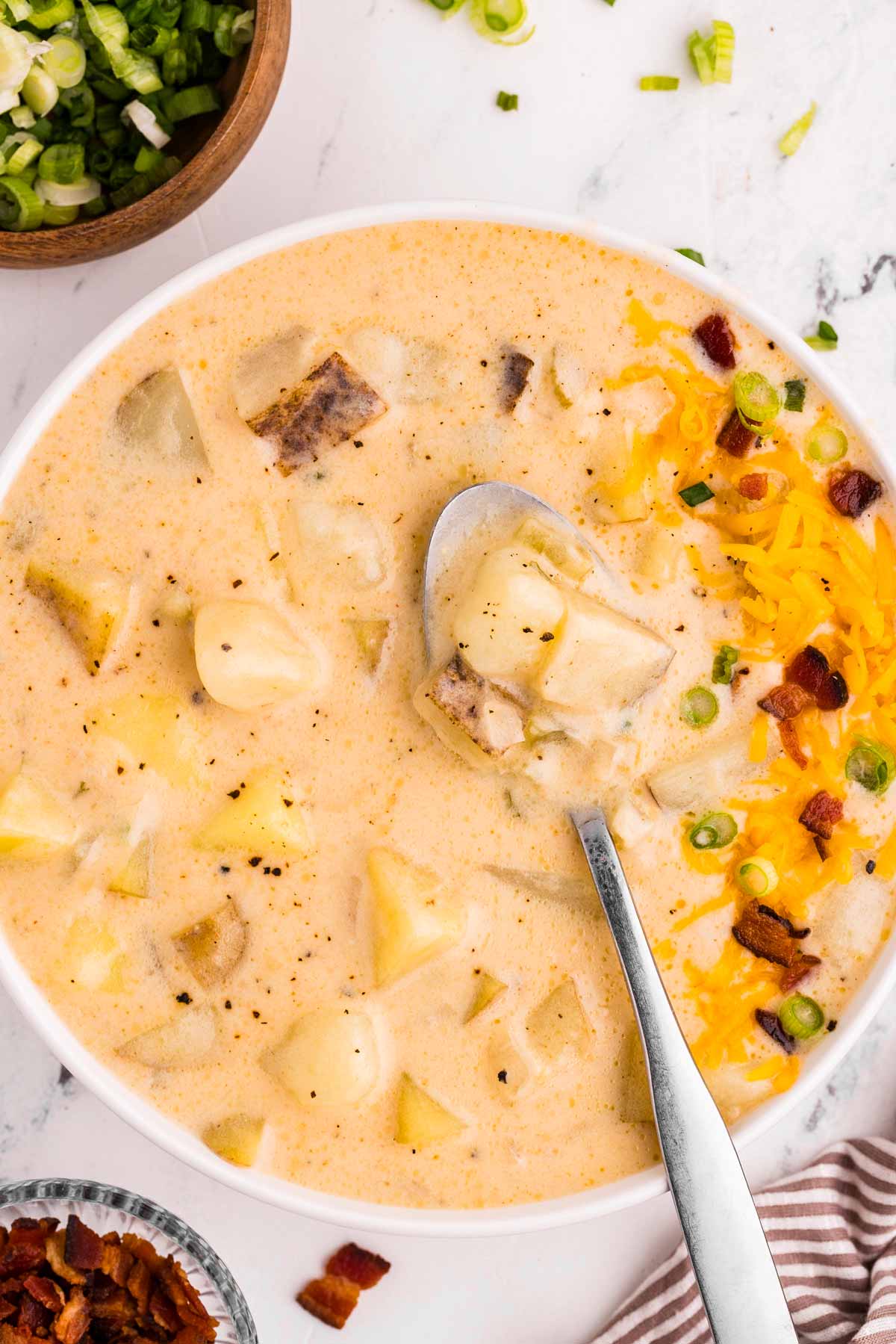 overhead view of creamy potato soup in a bowl, topped with crispy bacon, shredded cheese, and chives